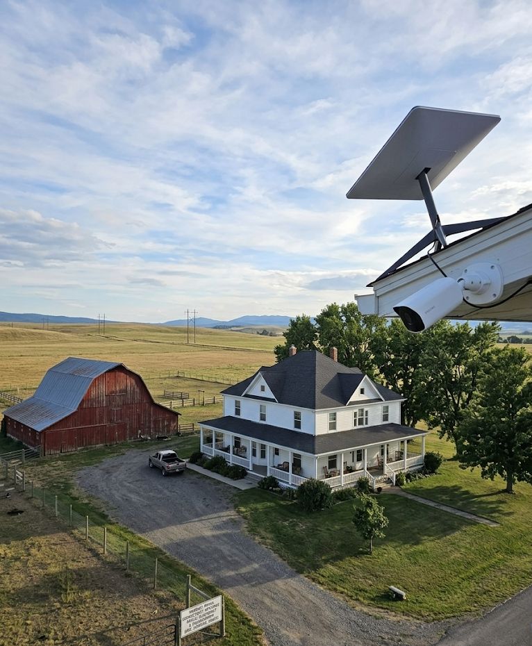 Starlink satellite dish and security camera mounted on a structure overlooking a rural farmhouse and barn